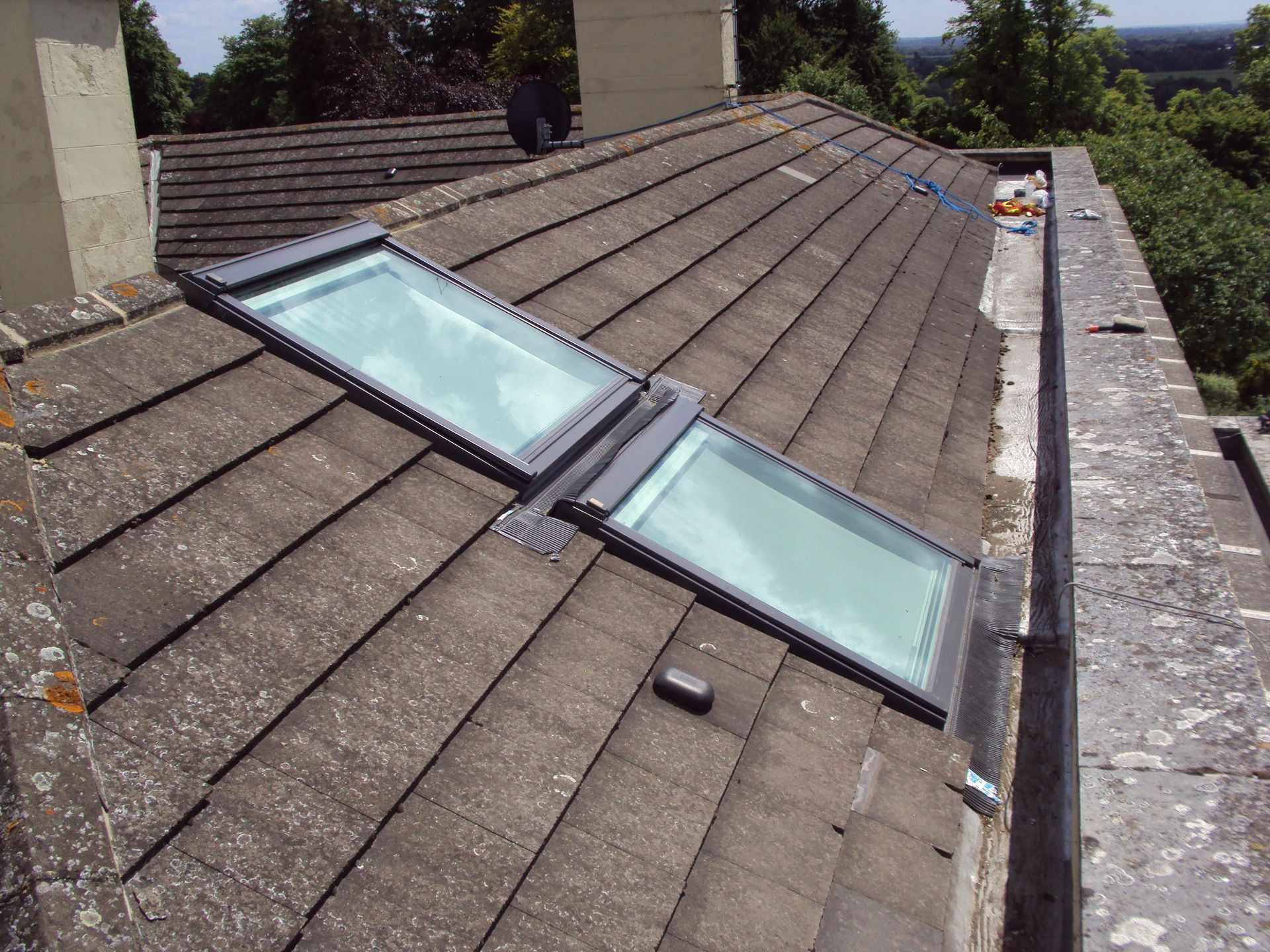 Two rectangular skylights on a tiled roof. The roof has lichen and is next to a stone wall.