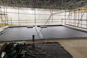 A flat roof covered in black material, possibly being worked on, with scaffolding surrounding the structure.