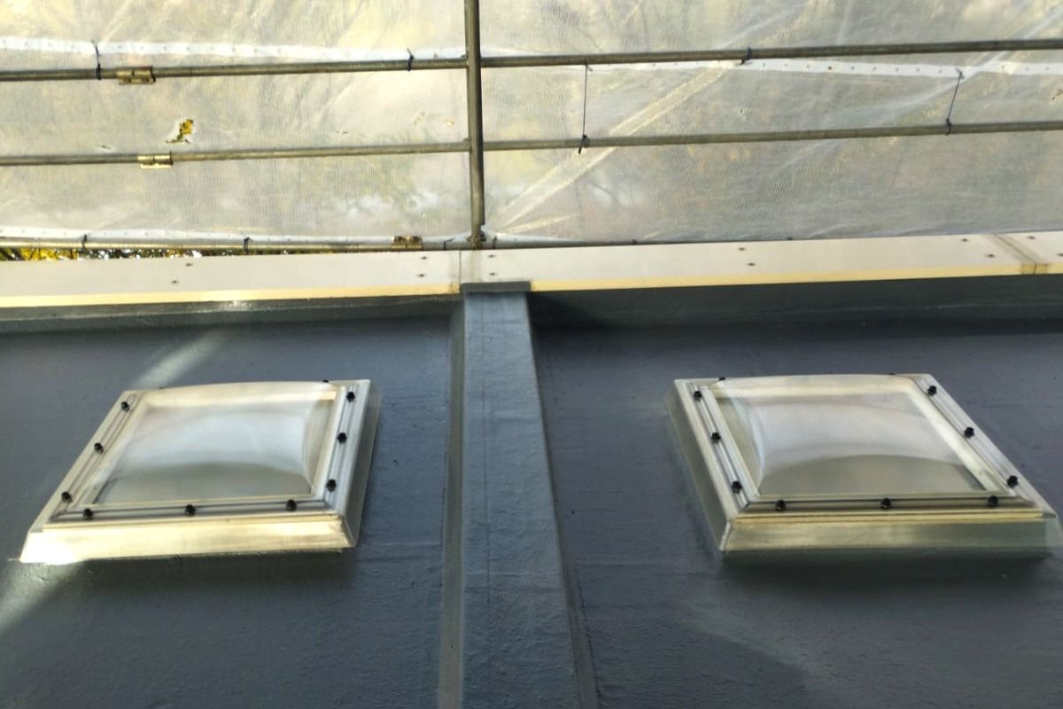 Two square skylights in a flat, gray rooftop, with a support beam between them. Gray backdrop.