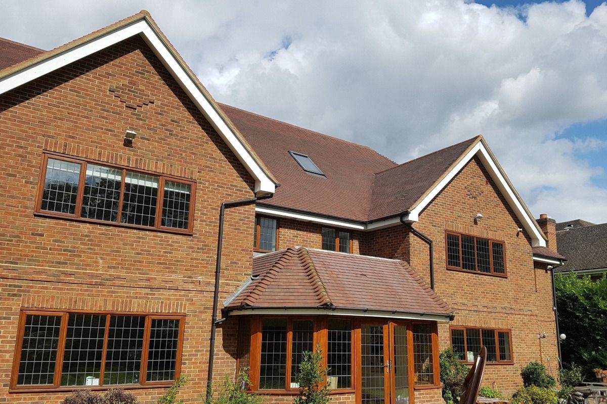 Red brick house with brown trim and roof tiles, featuring multiple windows and a sunny sky.