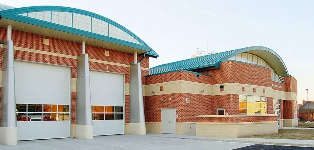 Exterior view of a modern brick fire station with a curved teal roof and open garage doors.