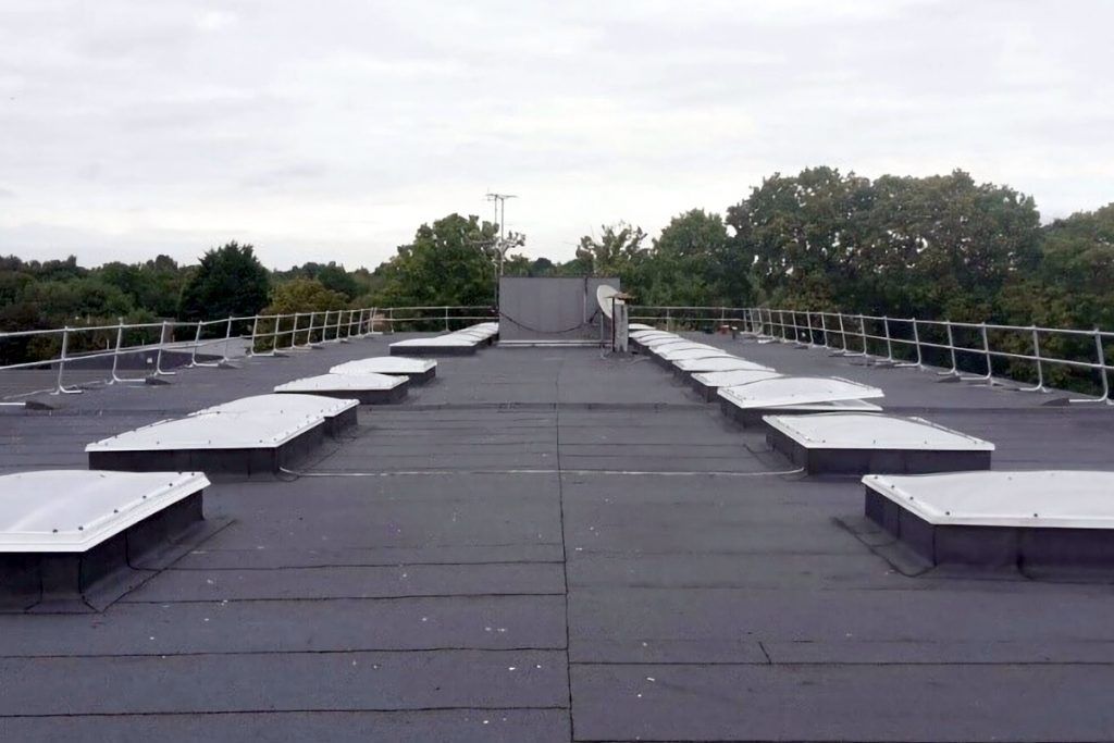 Flat, dark gray roof with numerous square skylights. Trees and a cloudy sky are in the background.
