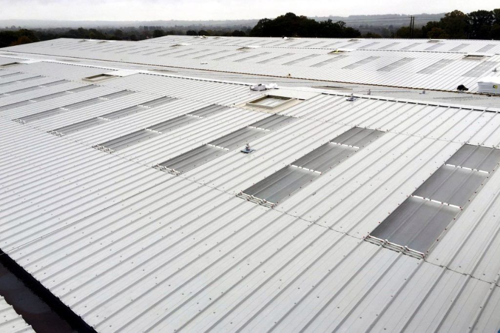 Aerial view of a large, white roof with many rows of skylights, likely a commercial building.