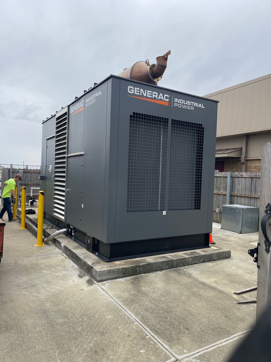 Gray GENERAC generator outside an industrial building, with workers nearby and a dog statue on top