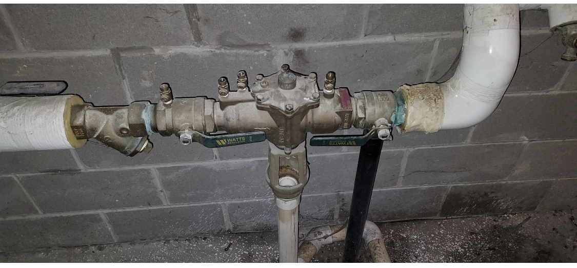 Water pressure regulator with pipes against a cinder block wall.