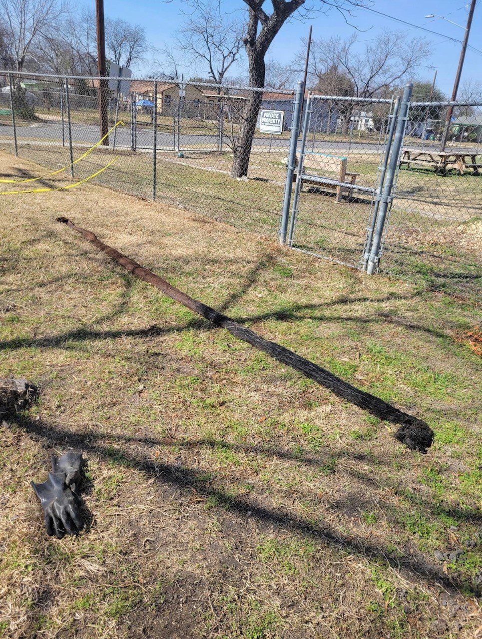 A charred cross-shaped structure lies on the grass in front of a chain-link fence.