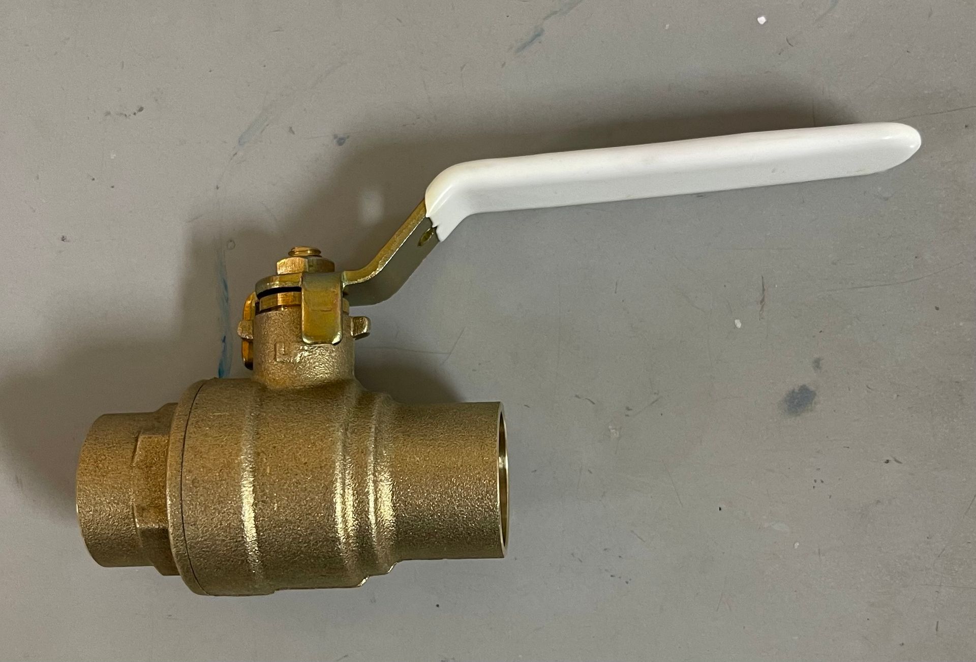 Brass ball valve with a white handle, lying on a gray surface.