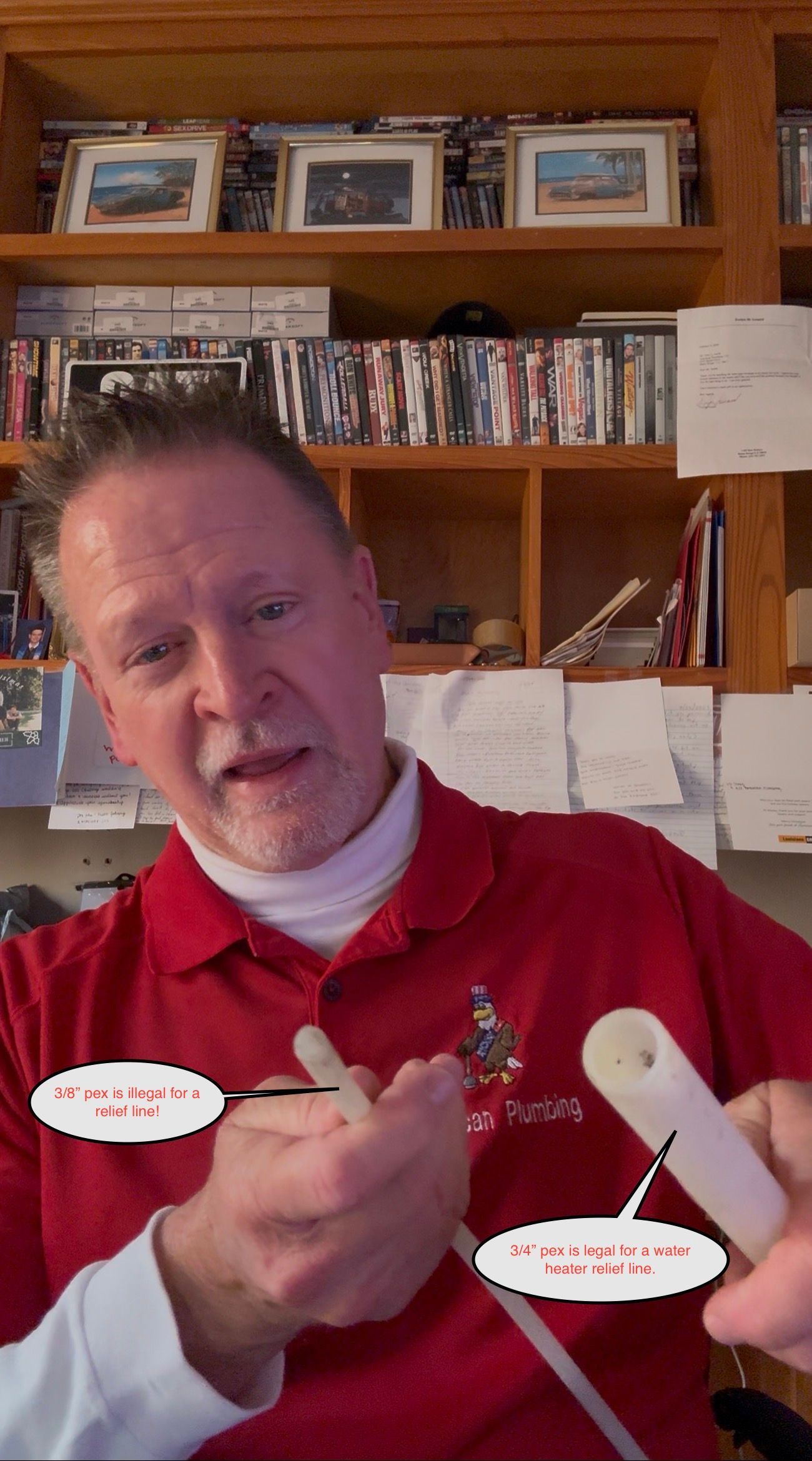 Man in red shirt gesturing with small objects in a home office, shelves and framed photos behind him
