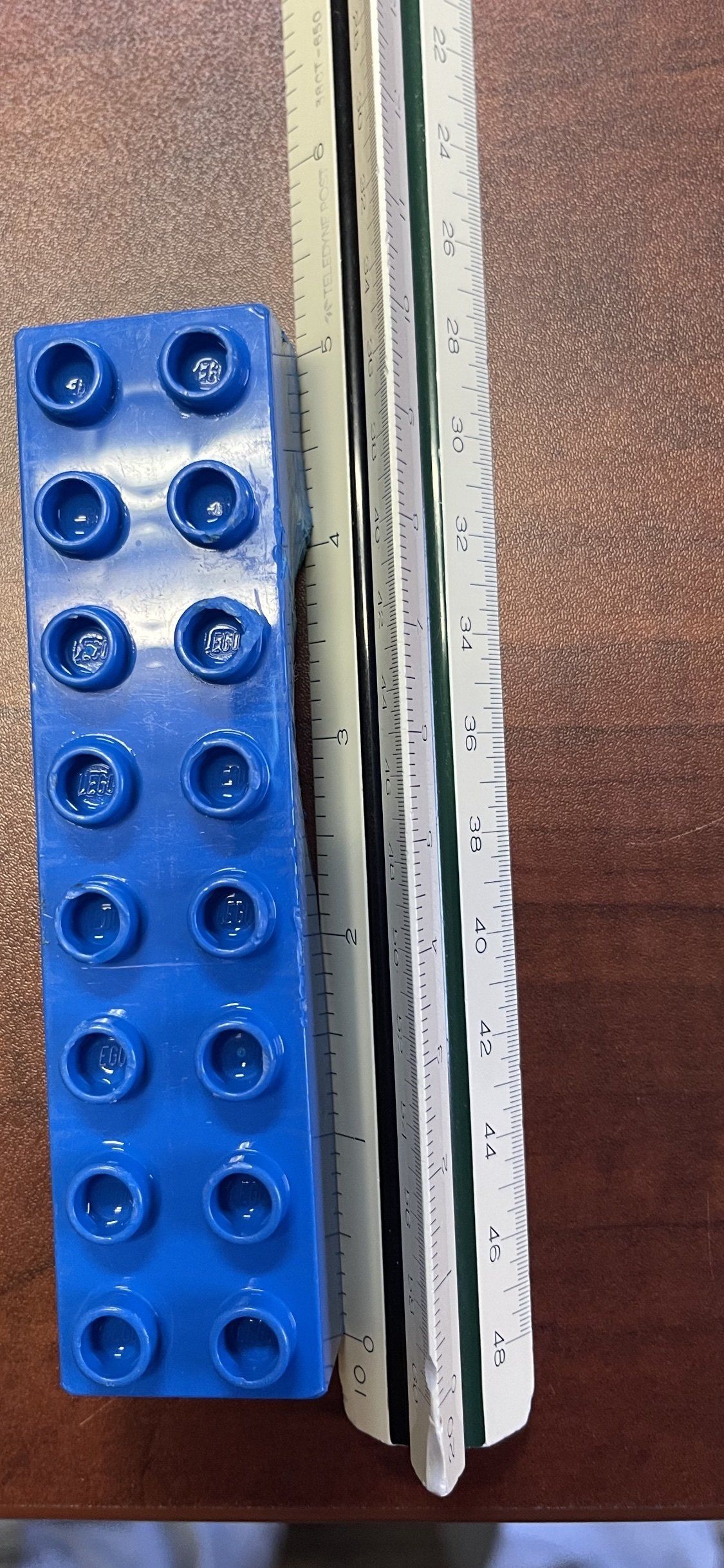 Blue LEGO brick next to a white and green striped object on a wooden surface.