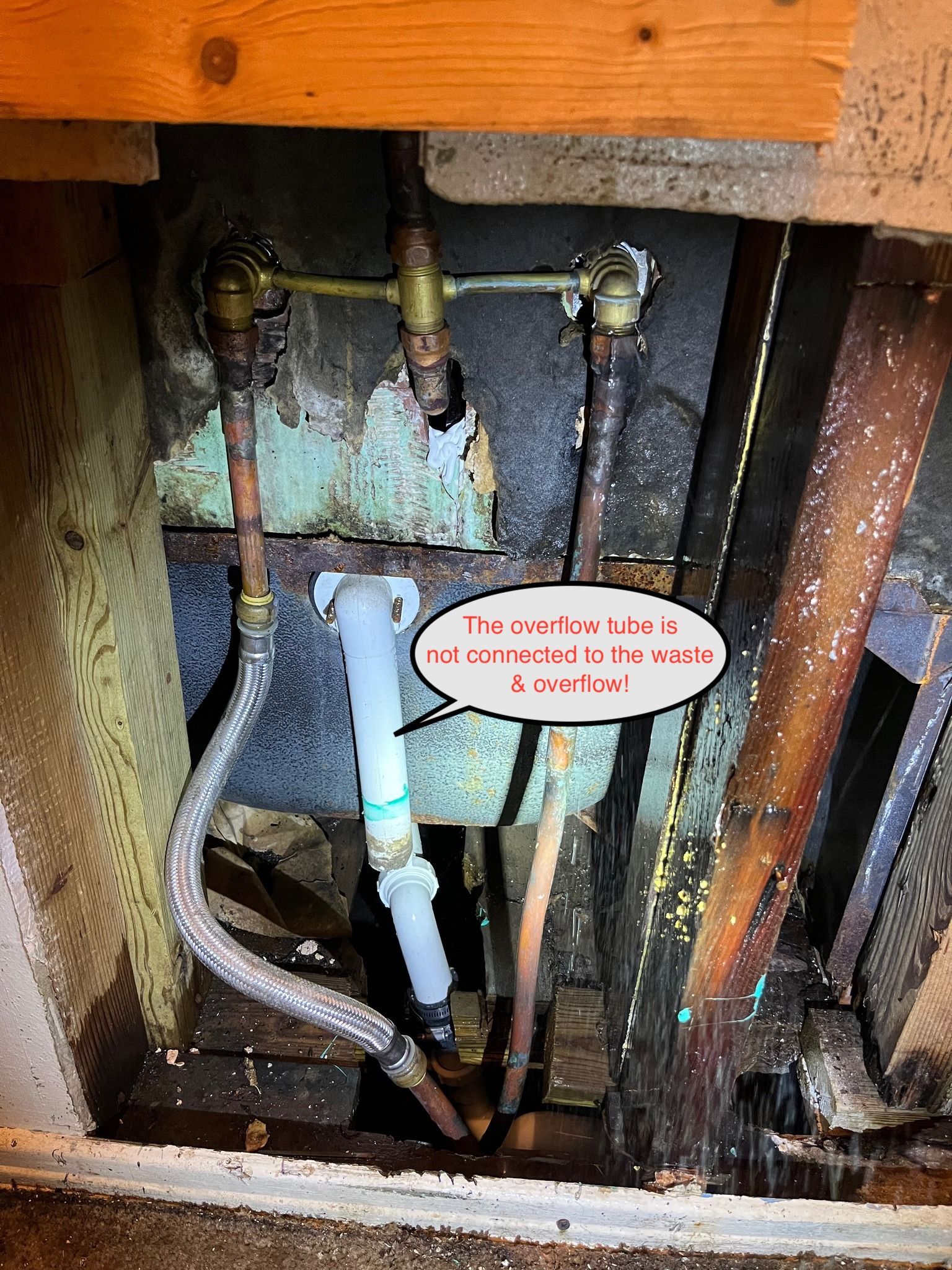 Exposed under-sink plumbing with a loose blue pipe and warning label inside a cabinet