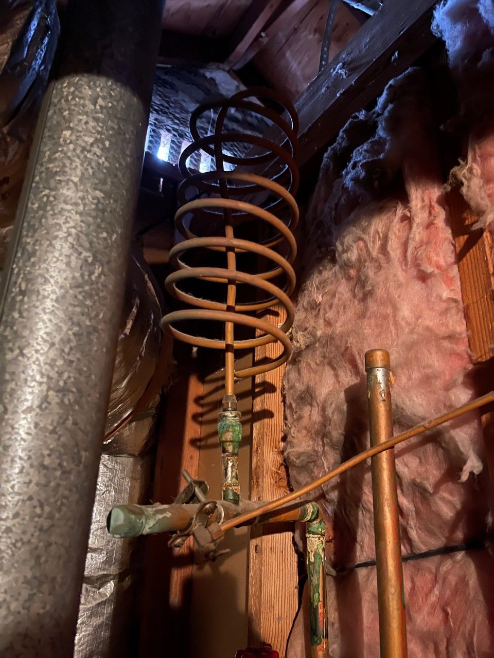 Orange coil spring and copper piping in an unfinished wall cavity with pink insulation