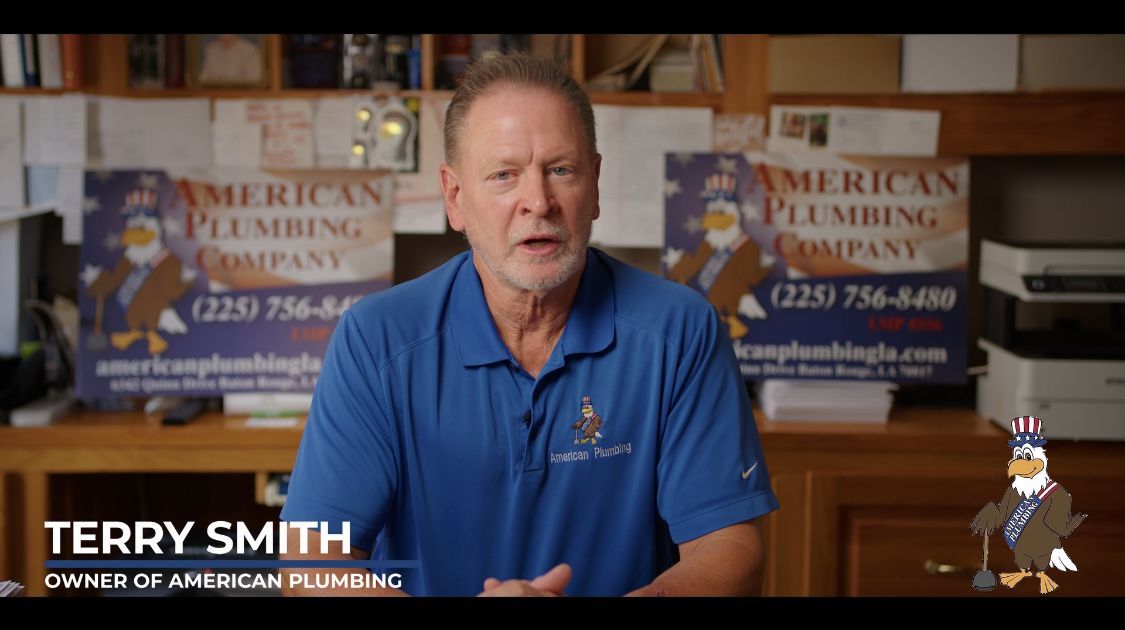 Terry Smith speaking in a blue shirt in a plumbing office, with American Plumbing signs in the background