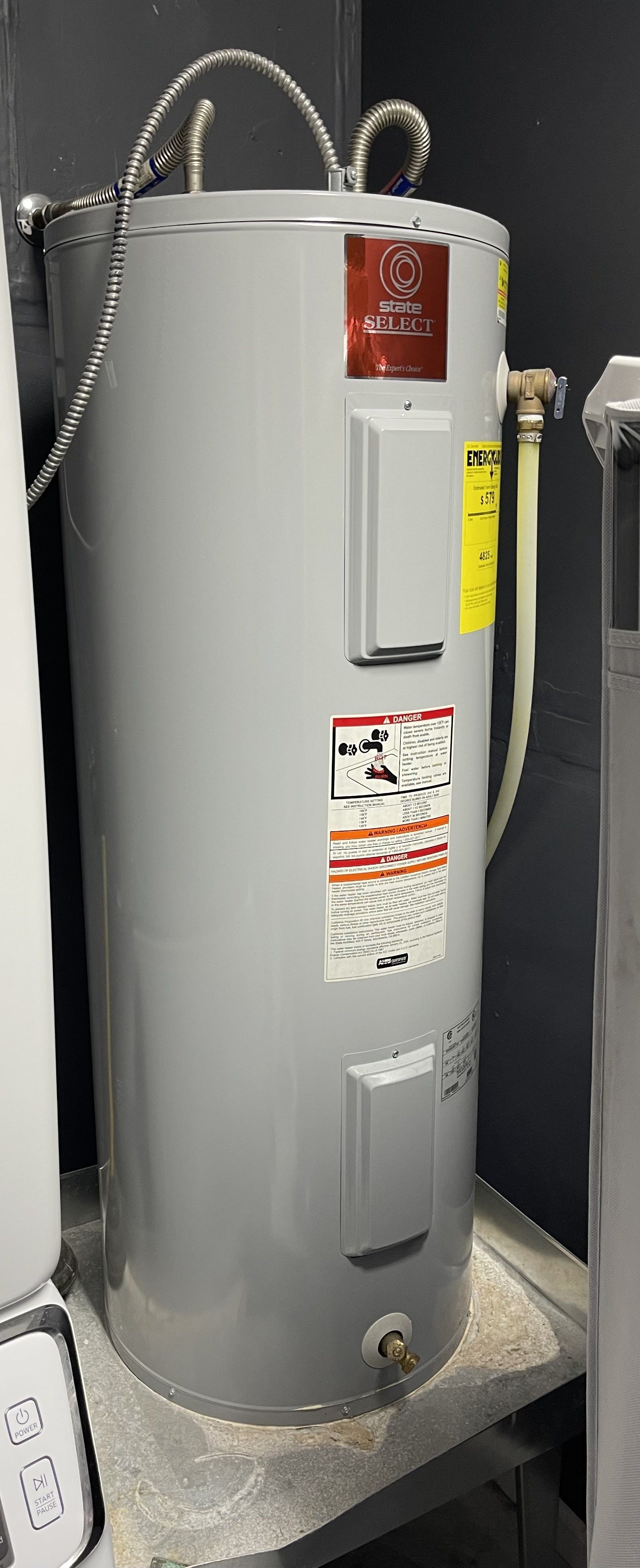 A tall, gray water heater in a utility room with pipes connected to the top.