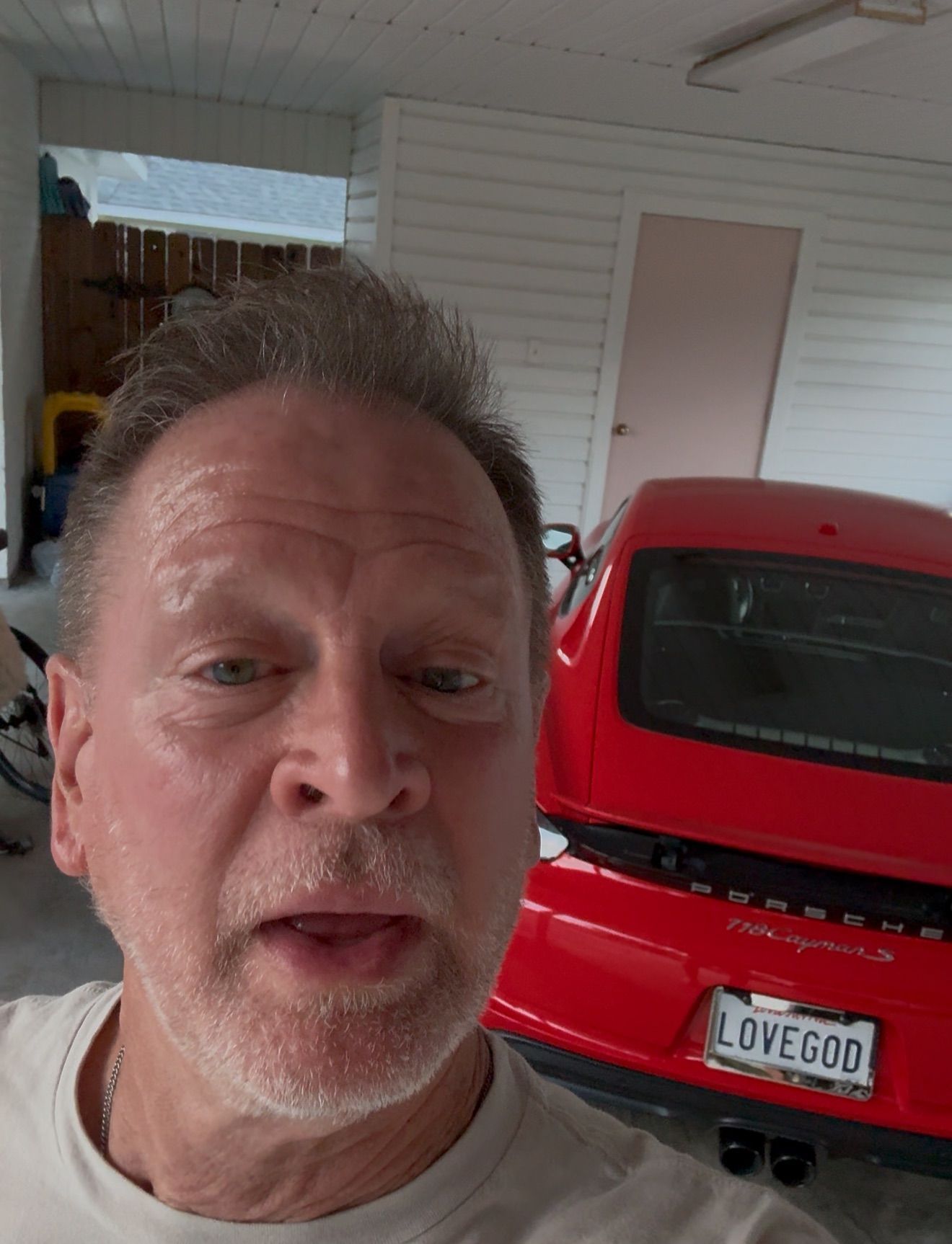 Man in a garage with a red Porsche; license plate reads