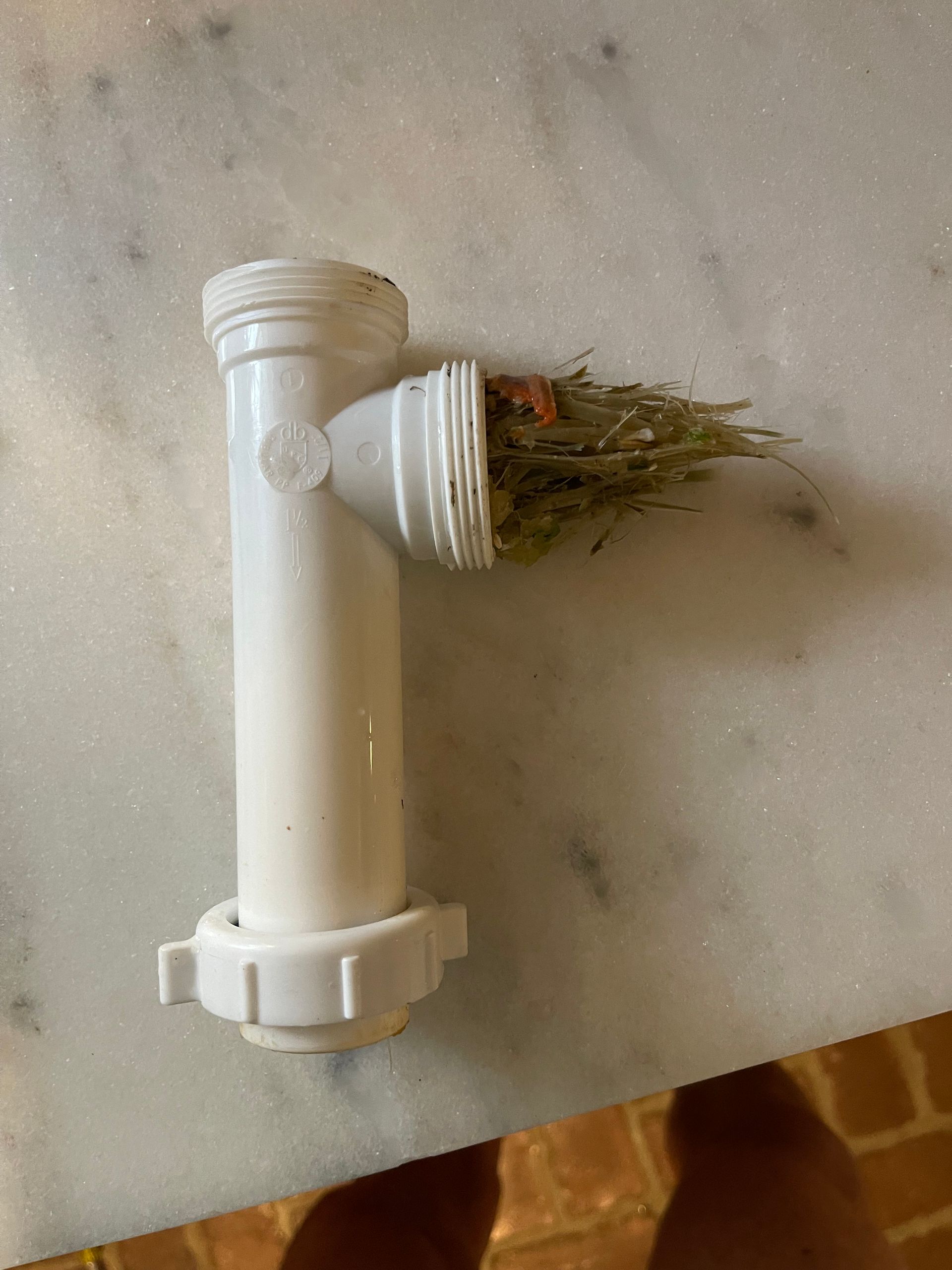 White PVC pipe fitting with a side branch holding dried grass on a marble countertop