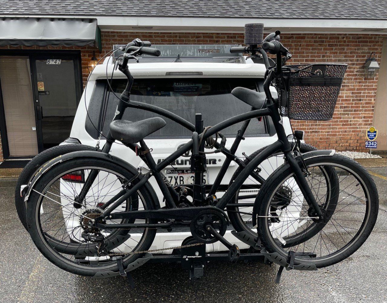 Two black bicycles mounted on a car rack parked in front of a brick building