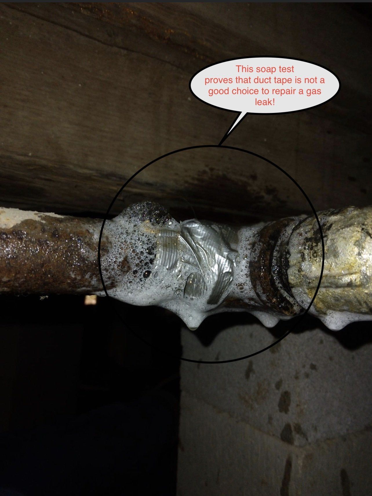Close-up of a rusty pipe joint with a white leak clamp under a wooden ceiling.