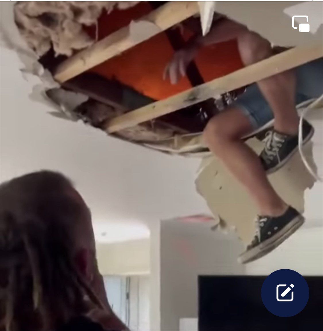 Man's legs dangle through a hole in the ceiling; someone watches from below.