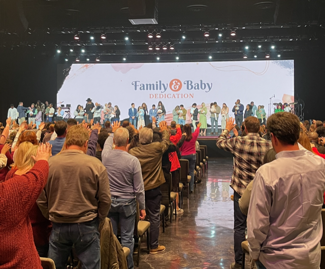 Audience standing and applauding at a “Family & Baby” stage event in a large conference hall