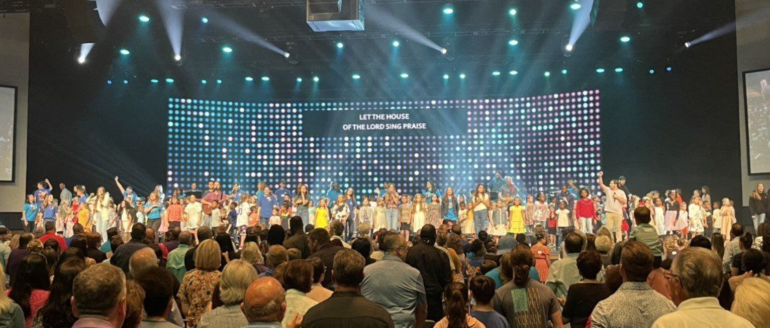 A choir on stage with a large audience; colorful clothing, bright lights.