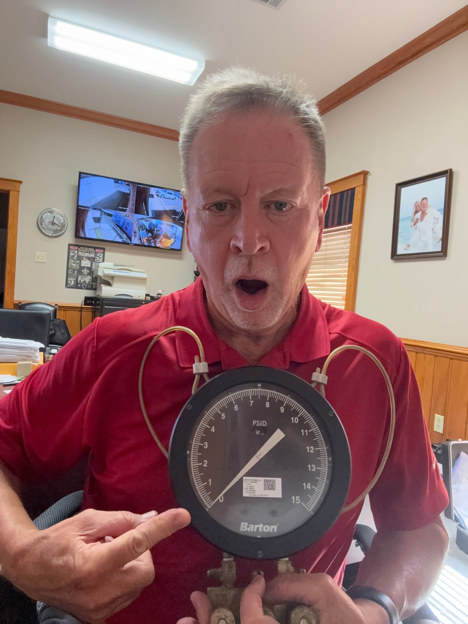 Man holding a red analog scale gauge toward the camera indoors