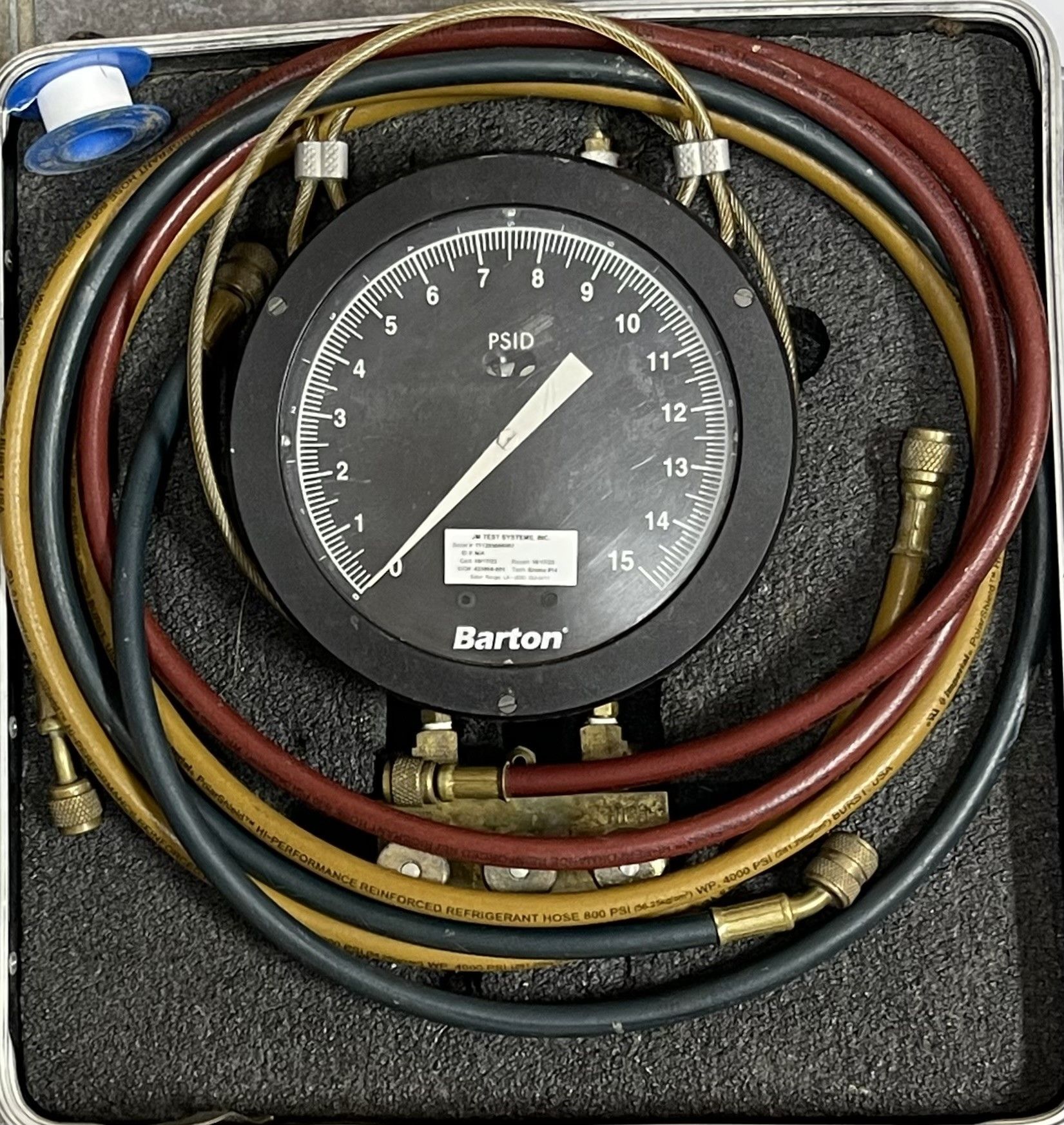 Coiled red and yellow hoses around a Barton gauge in a black foam case.
