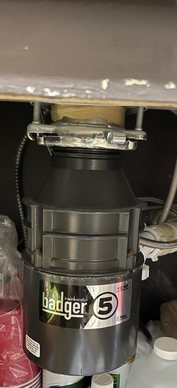 Badger 5 garbage disposal installed under a sink. Black and silver with a power cord.