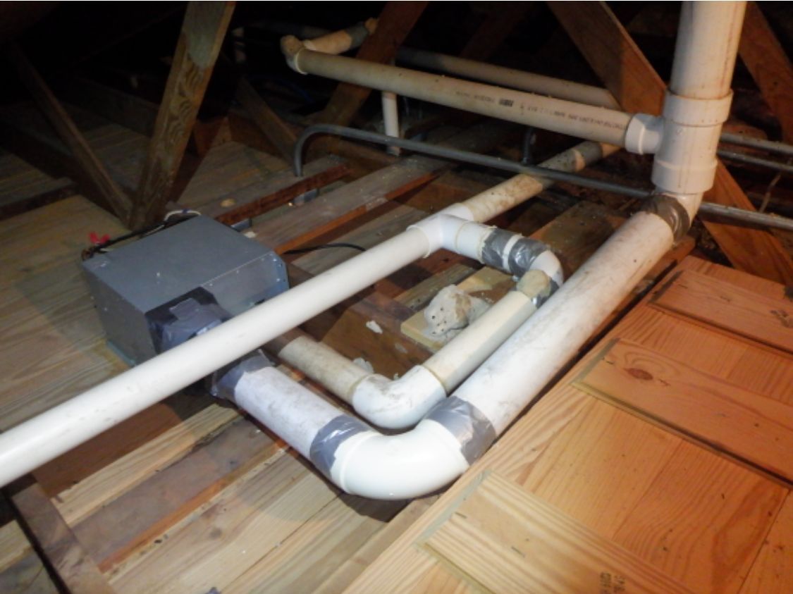 PVC pipes and a gray junction box beneath a wooden floor in an attic space