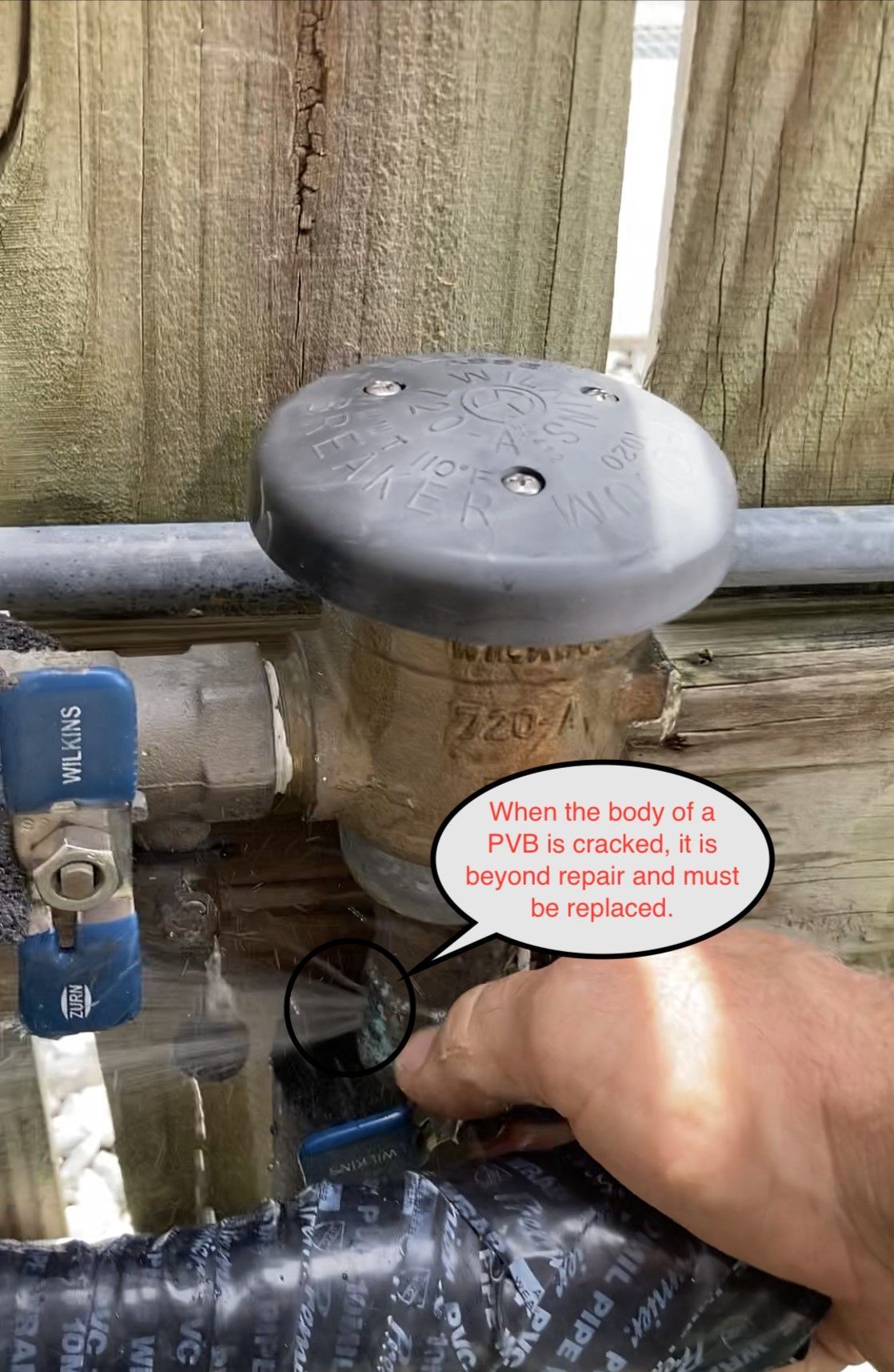 Person turning the valve on a backflow preventer near wooden fence.