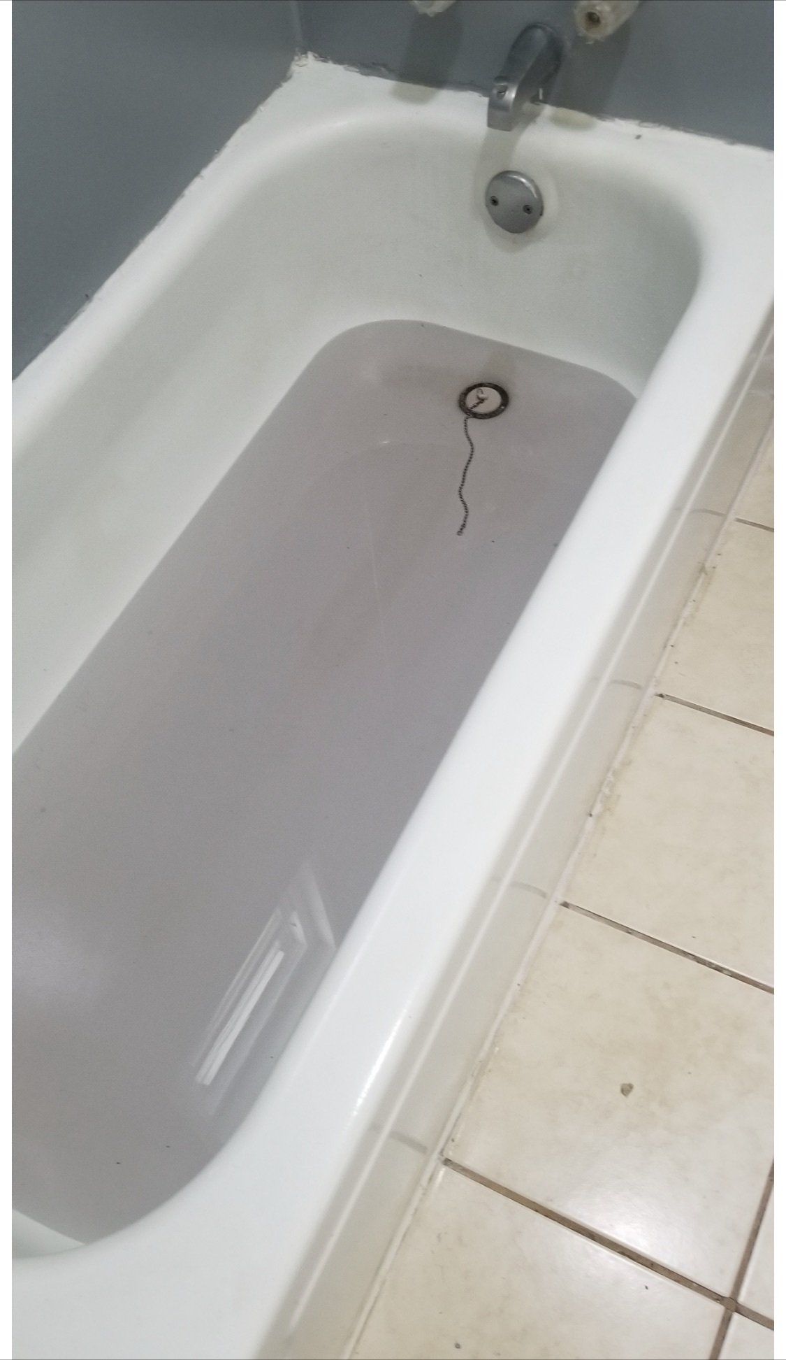 A bathtub filled with cloudy water, with a drain stopper chain hanging in the tub.