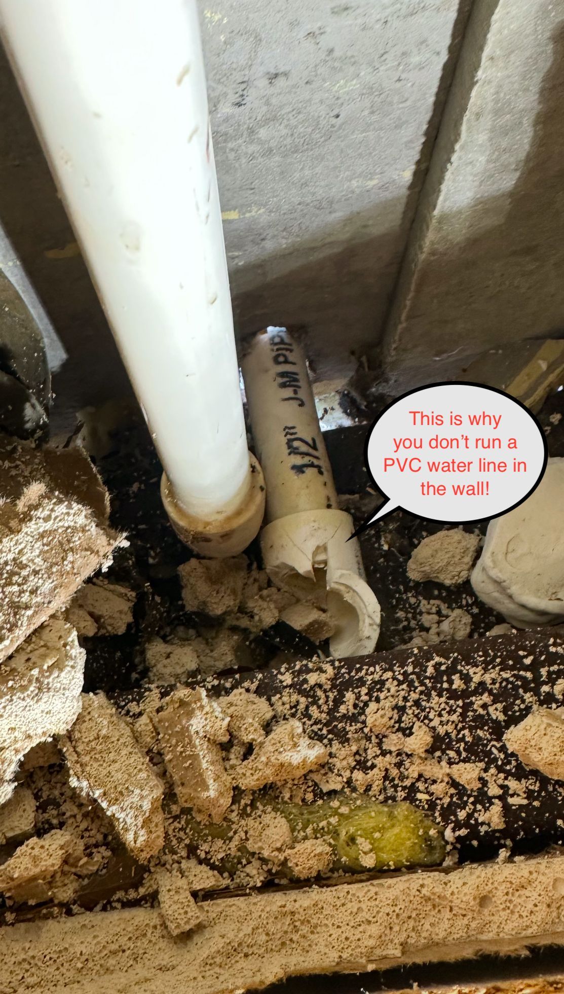 Dirty crawlspace pipes with moldy debris and a small sign near the plumbing