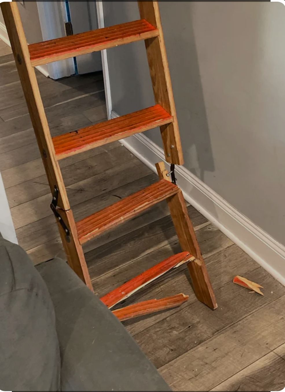 Damaged wooden ladder leaning against a wall, with a broken rung on the floor beside it.