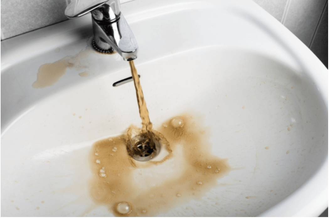 Brown water pours from a chrome faucet into a white sink.