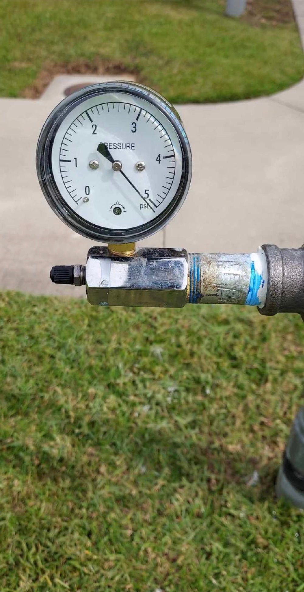 Pressure gauge mounted on a pipe, showing a low reading outdoors on grass.