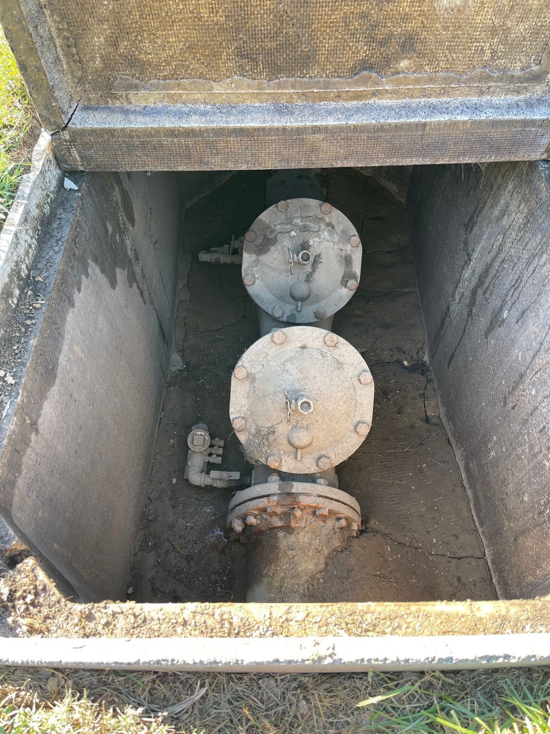 Open concrete utility box with two metal water valve covers.