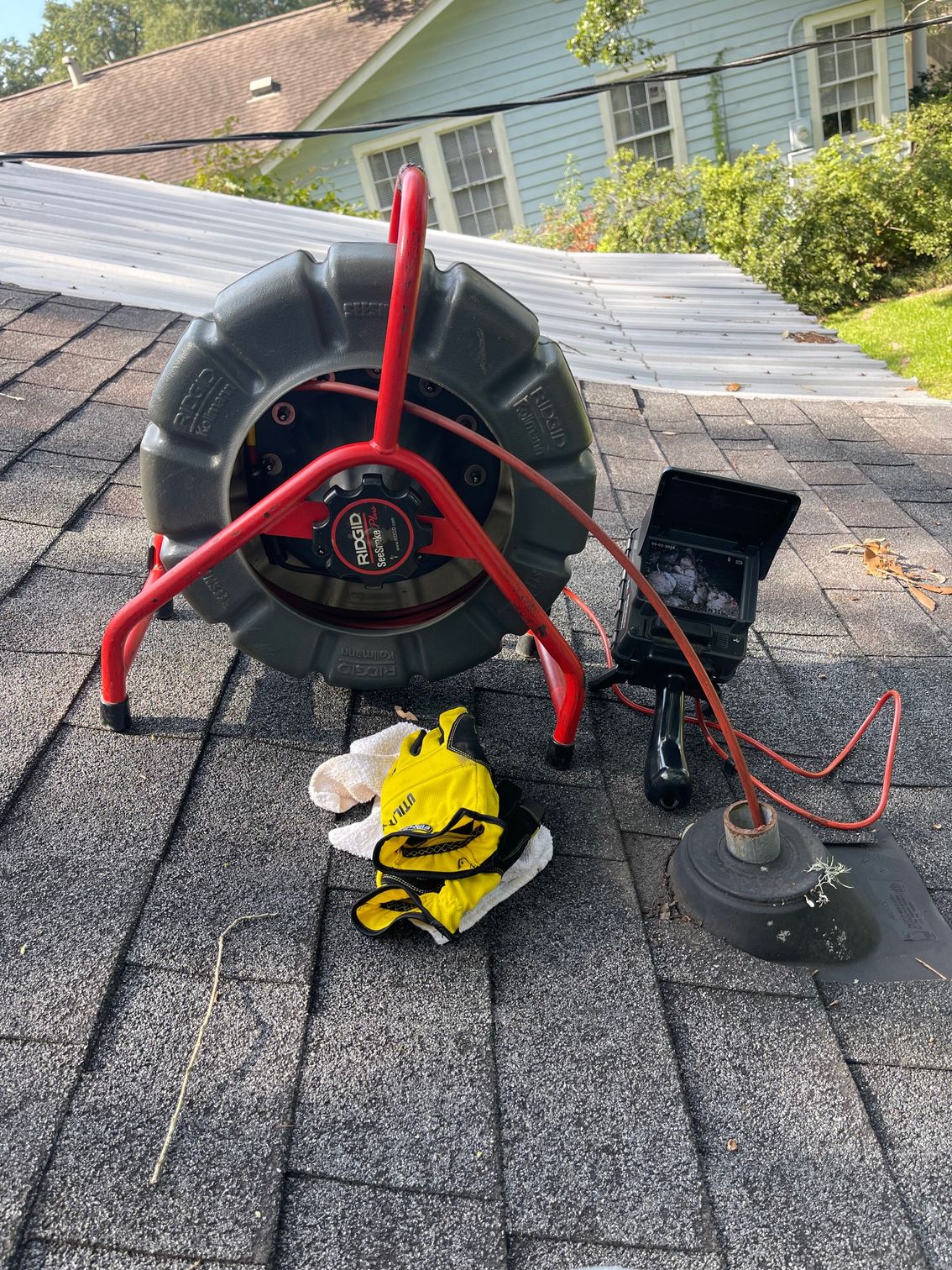 Red hose reel on a shingled rooftop beside a yellow safety vest and a black vent opening.