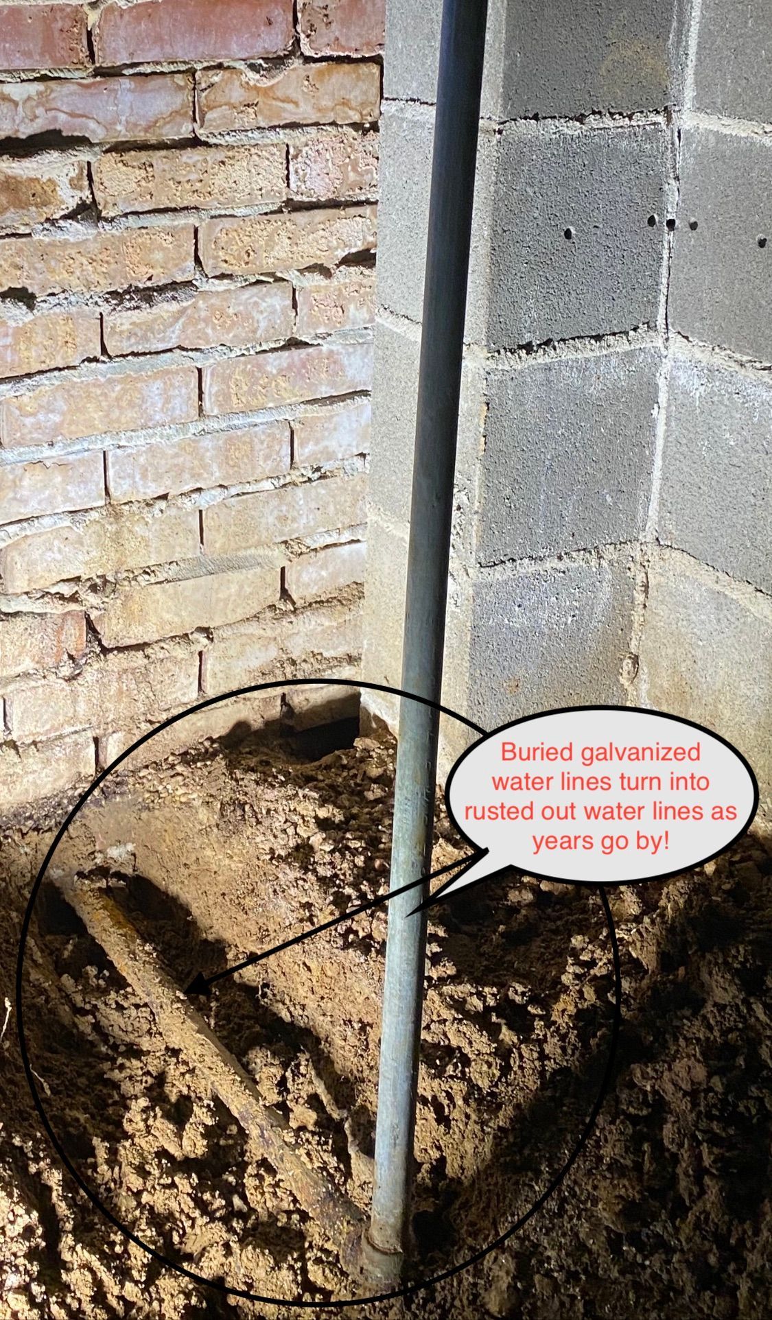 Construction pit beside brick and cinder block walls, with a white pipe in the dirt.