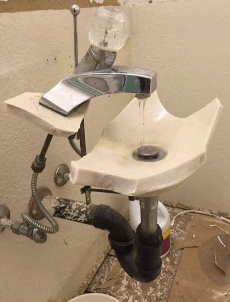 Broken white porcelain sink with detached faucet and exposed plumbing