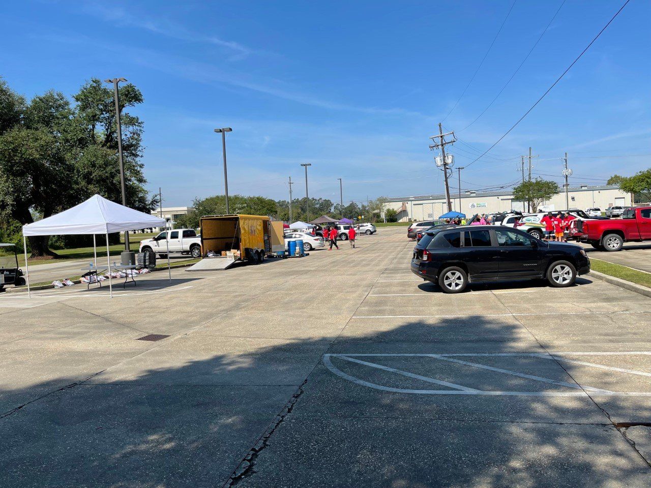 Outdoor parking lot with tents, cars, and people on a sunny day