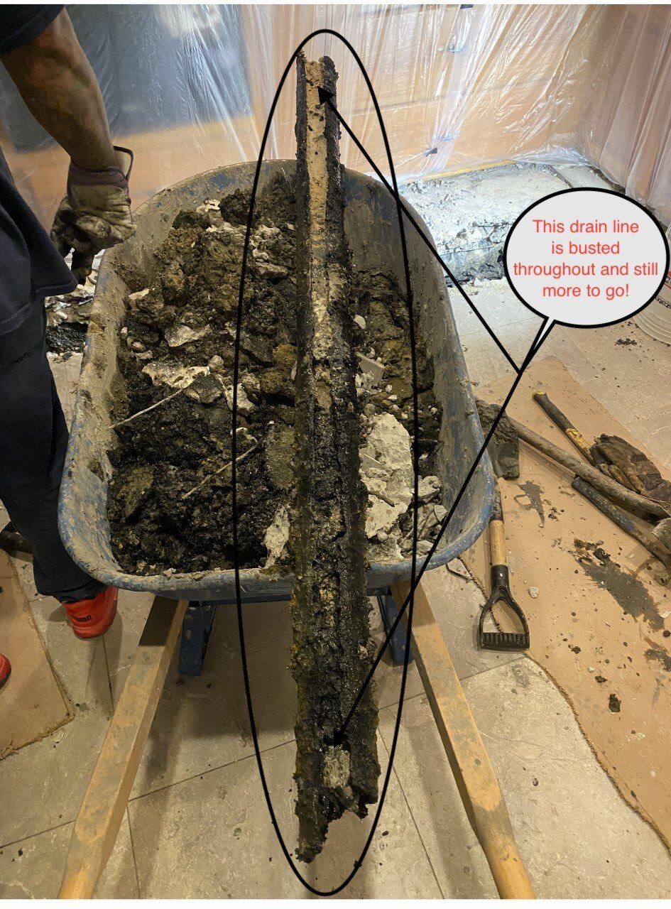 Wheelbarrow of debris, including a long, wooden beam, with a worker's hands and feet visible.