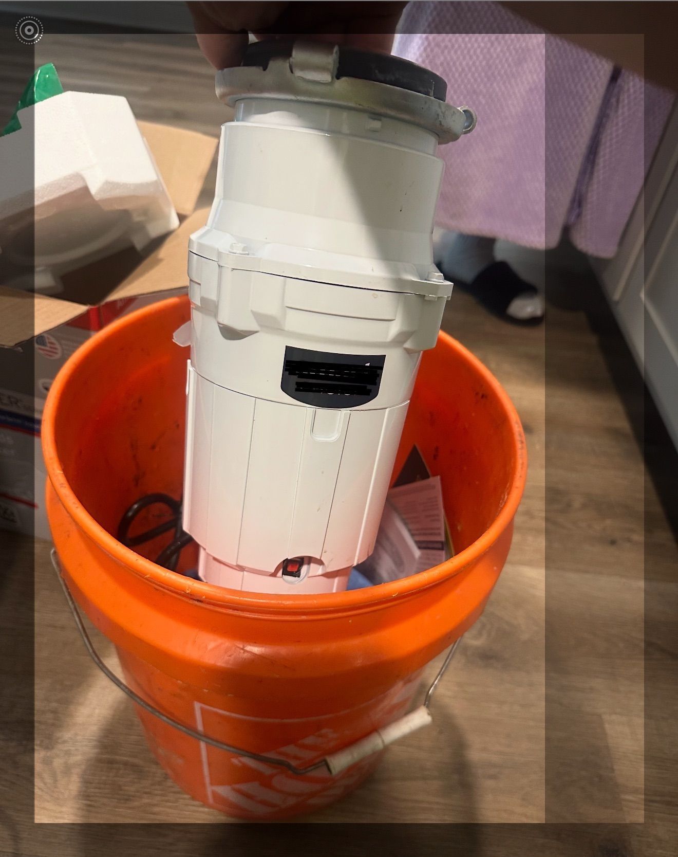 White appliance leaning in an orange bucket on a wooden floor, with purple curtains in the background