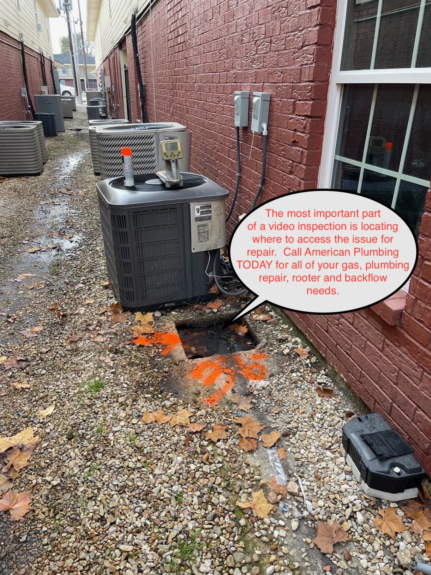 Backyard HVAC unit by brick wall with orange spray paint marking on gravel ground