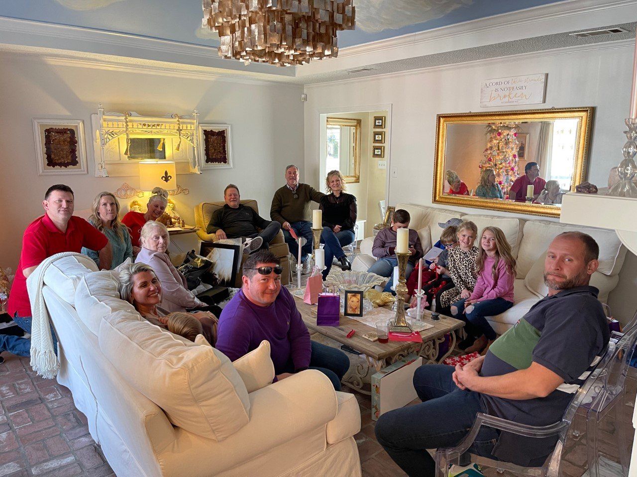 People gathered in a bright living room, seated on sofas and chairs around a coffee table.