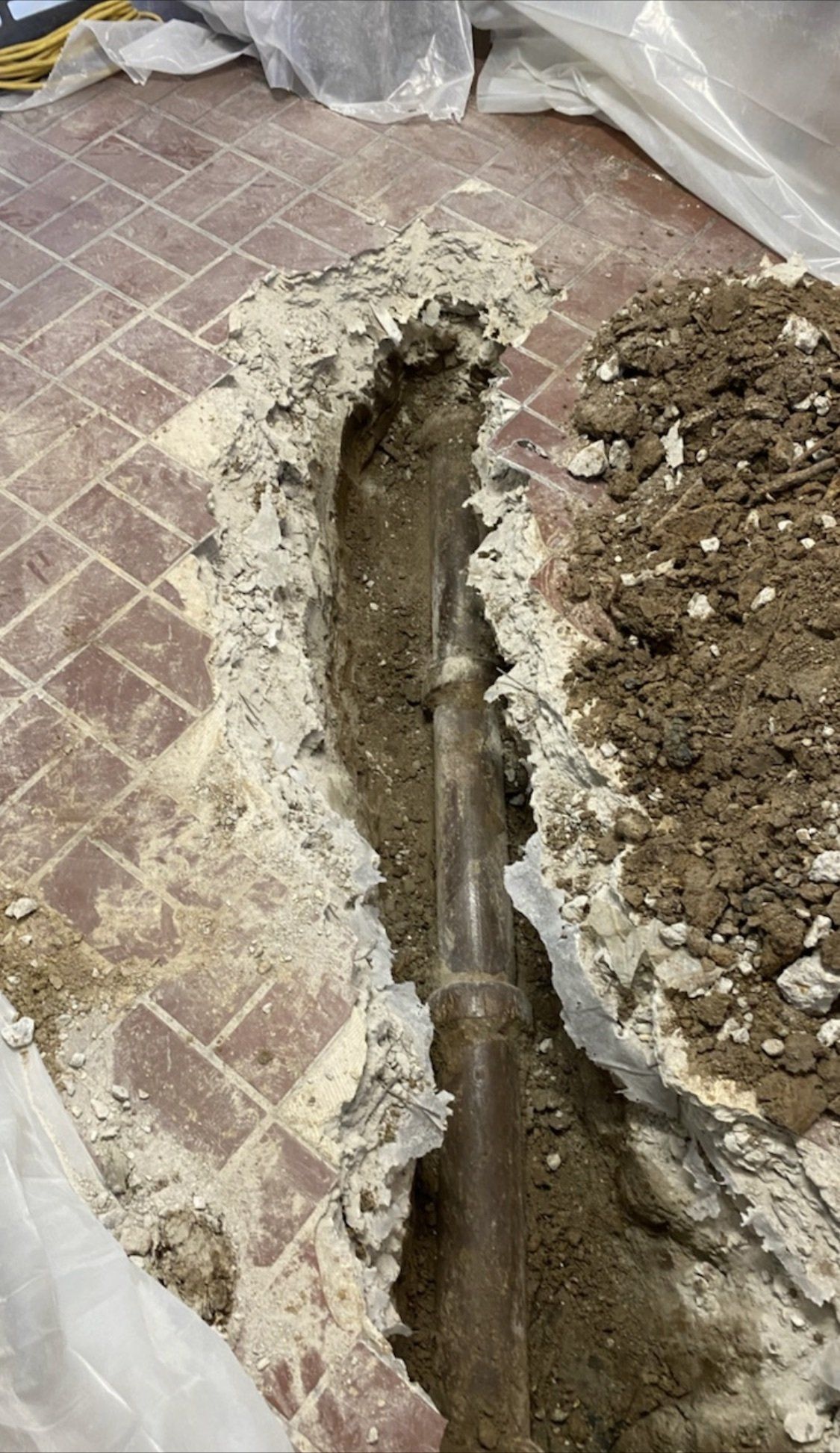 Broken floor exposing a deep trench, with rubble piled along one side indoors
