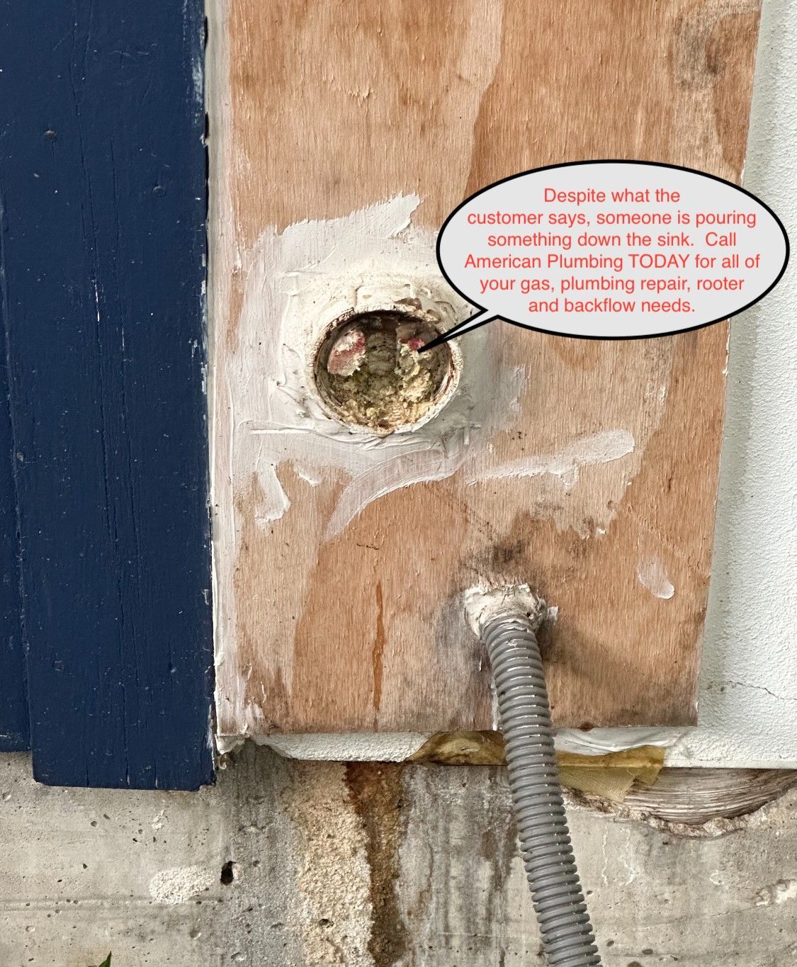 Damaged wooden board with an empty hole and a corrugated metal conduit near a wall corner