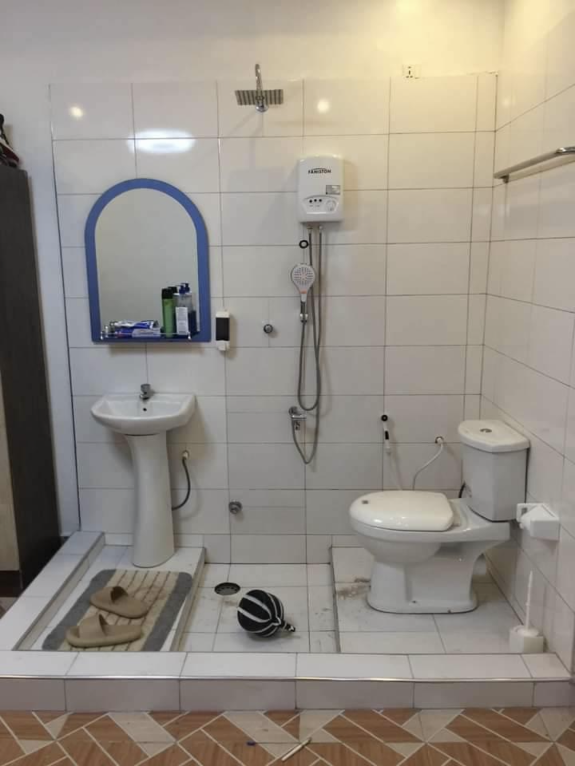 Small tiled bathroom with sink, mirror, shower, toilet, and bath mat.