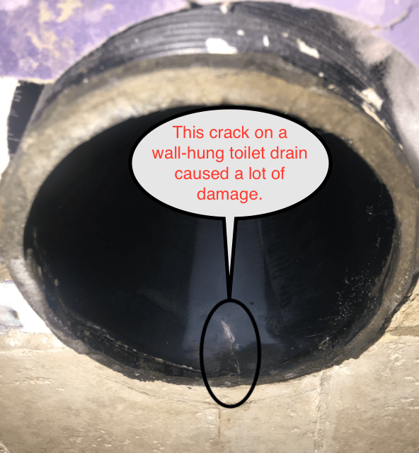 Close-up of a cracked wall-hung toilet drain causing damage.