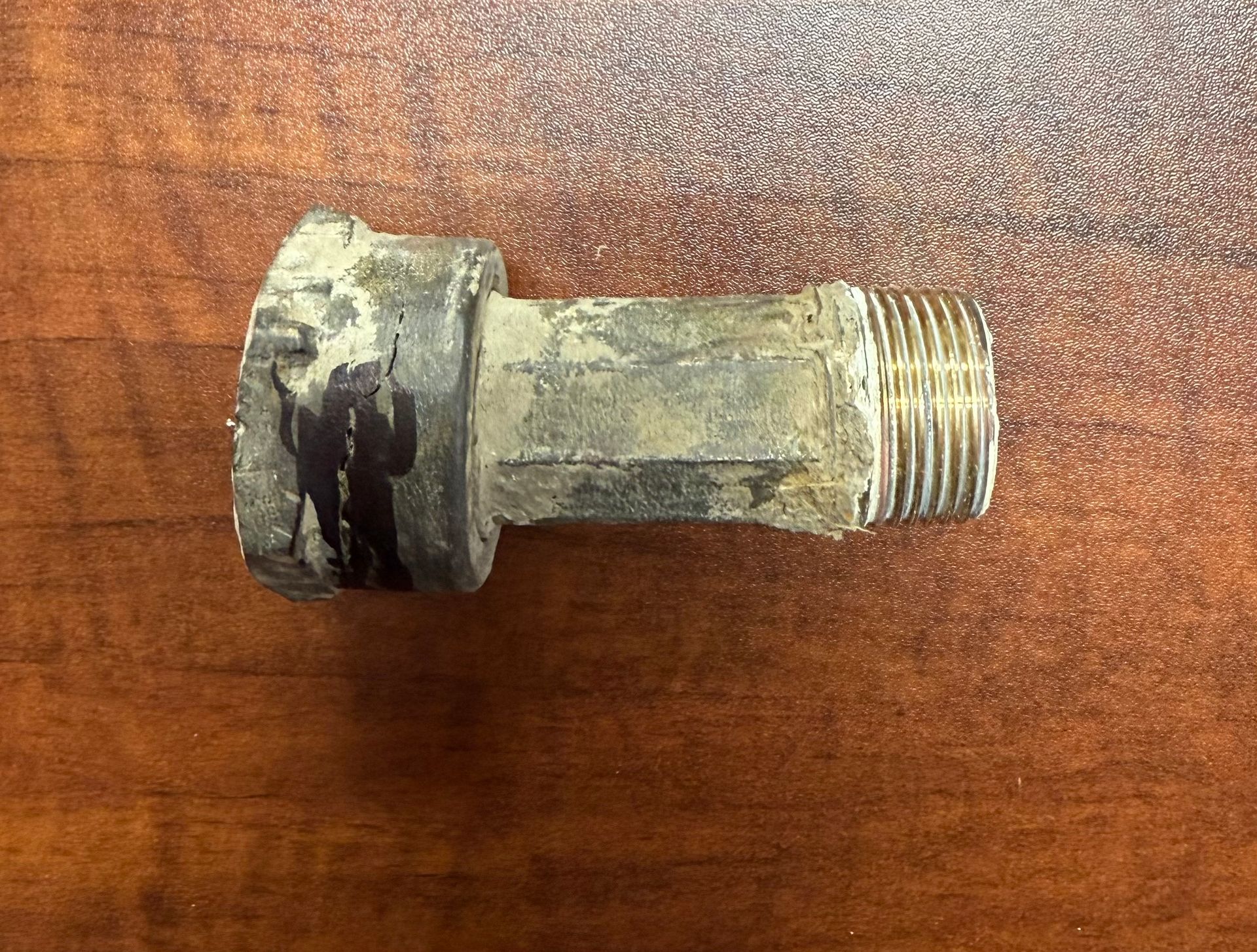 Worn metal pipe fitting with threaded end on a wooden surface