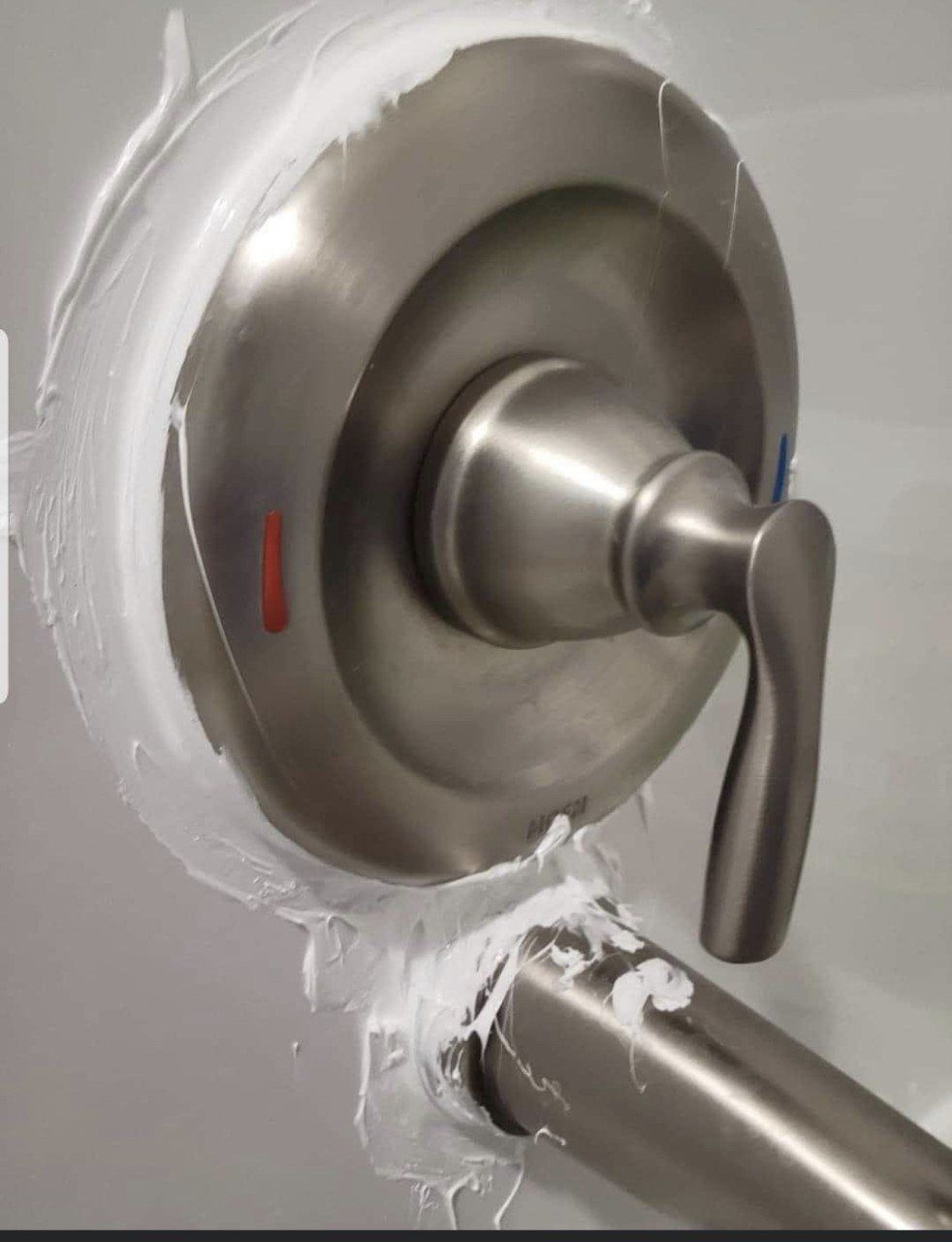 Silver shower valve handle with white sealant around the plate and pipe opening.