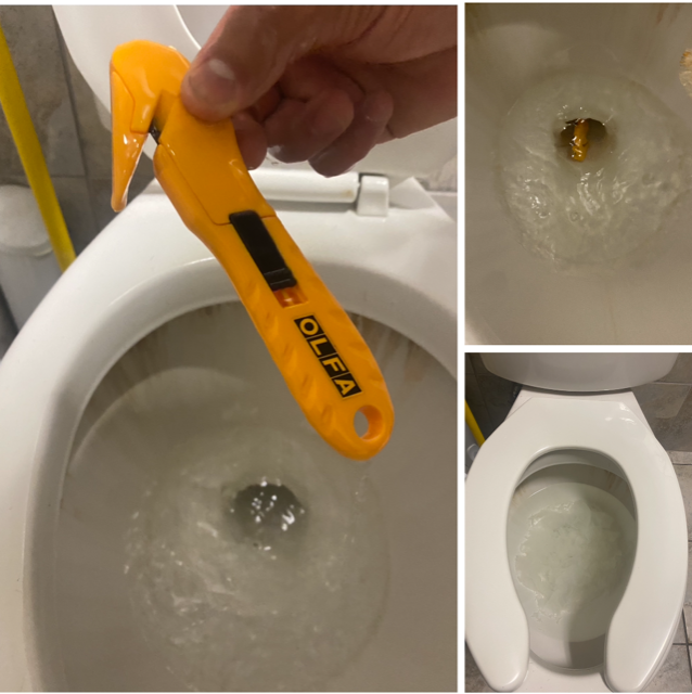 Hand holding yellow utility knife over a toilet bowl with a clogged drain and bubbling water